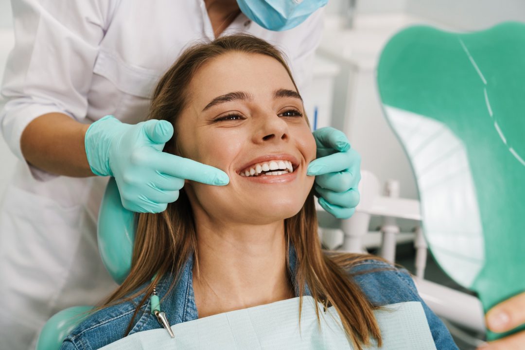 european-young-woman-smiling-while-looking-at-mirror-in-dental-clinic